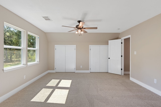 unfurnished bedroom with ceiling fan, vaulted ceiling, two closets, and light colored carpet