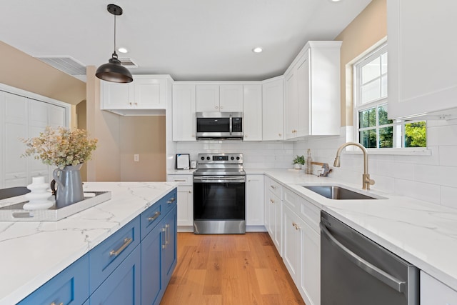 kitchen with stainless steel appliances, sink, decorative light fixtures, light wood-type flooring, and blue cabinets