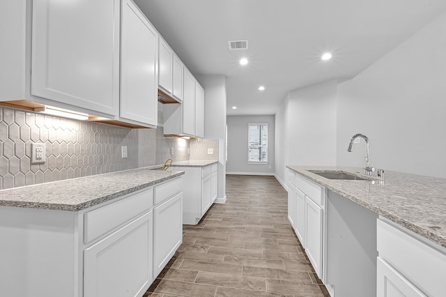 kitchen with light stone countertops, sink, white cabinets, and light hardwood / wood-style floors