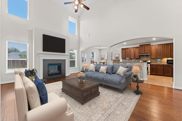 living room with ceiling fan, high vaulted ceiling, and light hardwood / wood-style flooring