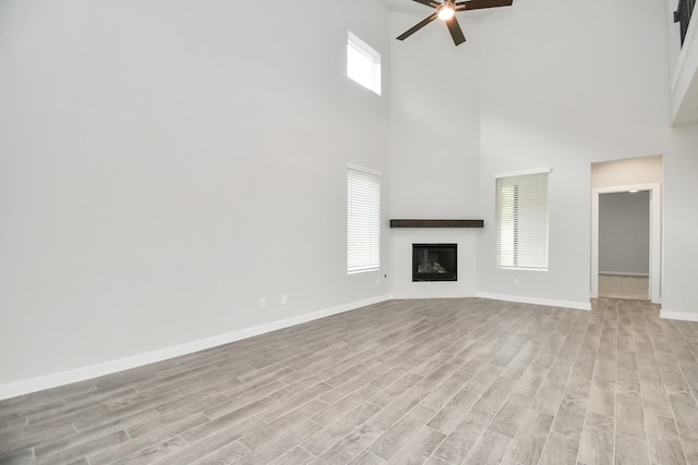 unfurnished living room with ceiling fan, a high ceiling, and light wood-type flooring