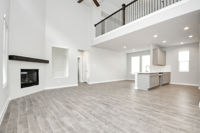 unfurnished living room featuring light hardwood / wood-style flooring, a high ceiling, and ceiling fan