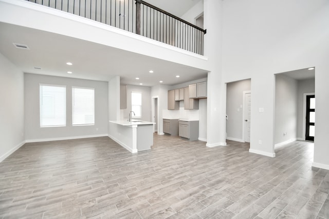 unfurnished living room with light hardwood / wood-style floors, a towering ceiling, and sink