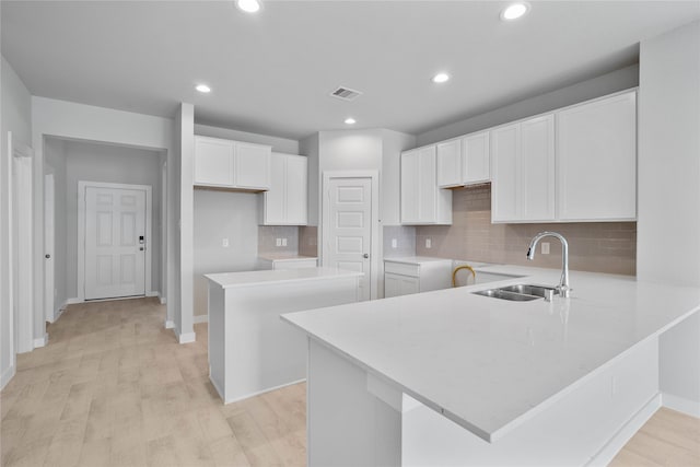 kitchen featuring sink, backsplash, light hardwood / wood-style flooring, a center island, and white cabinets