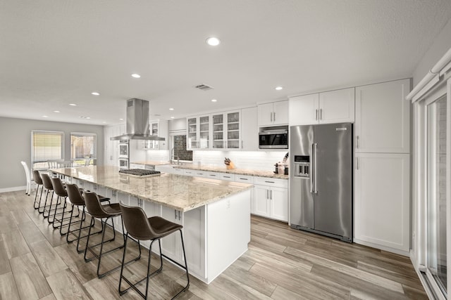 kitchen featuring appliances with stainless steel finishes, a spacious island, white cabinetry, range hood, and light stone counters