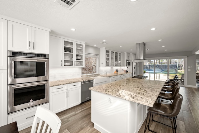 kitchen with sink, a kitchen island, island range hood, stainless steel appliances, and white cabinets