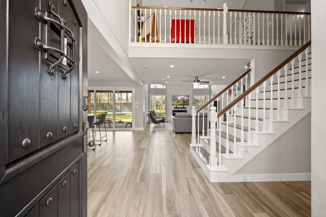 entryway with a towering ceiling, a fireplace, light wood-type flooring, and ceiling fan