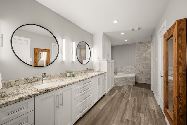 bathroom featuring vanity, wood-type flooring, and tiled bath