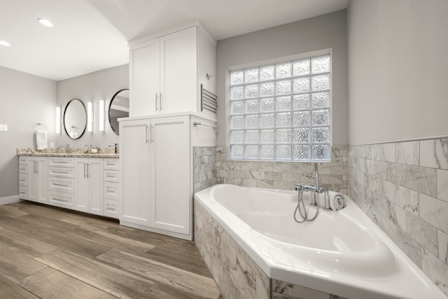 bathroom featuring vanity, hardwood / wood-style flooring, and a relaxing tiled tub