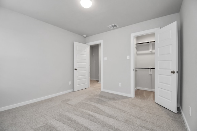 unfurnished bedroom with a closet, light colored carpet, and a walk in closet