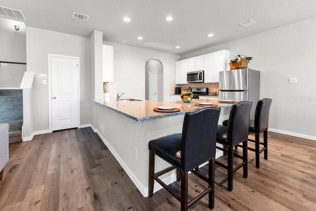 kitchen with white cabinets, appliances with stainless steel finishes, sink, a kitchen breakfast bar, and kitchen peninsula