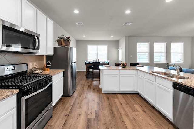 kitchen with white cabinetry, appliances with stainless steel finishes, light wood-type flooring, light stone countertops, and sink