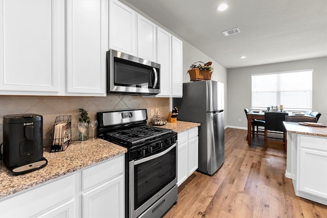 kitchen featuring backsplash, light hardwood / wood-style flooring, stainless steel appliances, white cabinets, and light stone counters