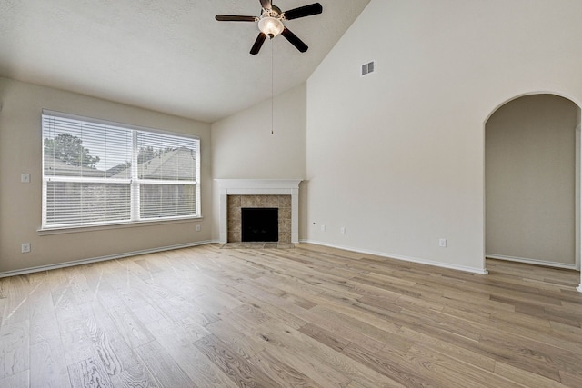 unfurnished living room with light hardwood / wood-style flooring, a tiled fireplace, high vaulted ceiling, and ceiling fan