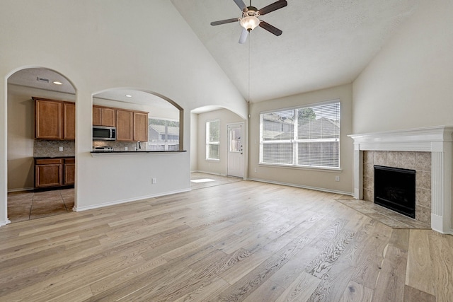 unfurnished living room with light hardwood / wood-style floors, high vaulted ceiling, a fireplace, and ceiling fan