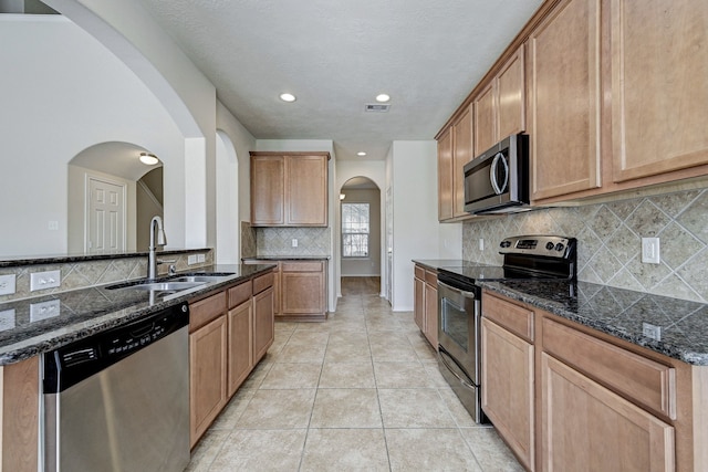 kitchen featuring dark stone countertops, sink, light tile patterned floors, appliances with stainless steel finishes, and tasteful backsplash