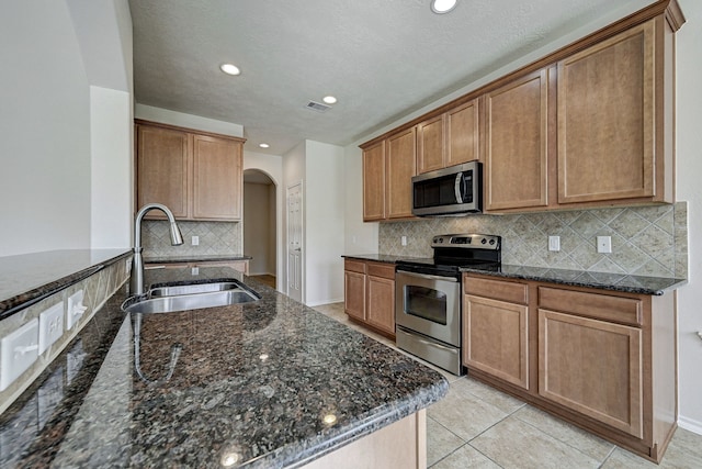 kitchen with dark stone countertops, sink, light tile patterned flooring, appliances with stainless steel finishes, and tasteful backsplash