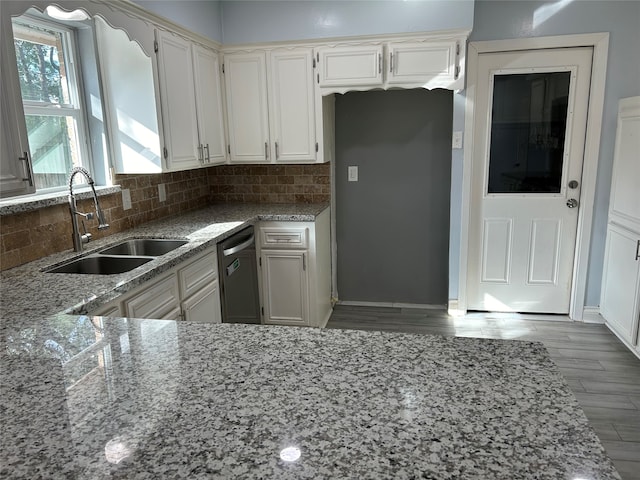 kitchen with light stone countertops, decorative backsplash, stainless steel dishwasher, sink, and white cabinetry