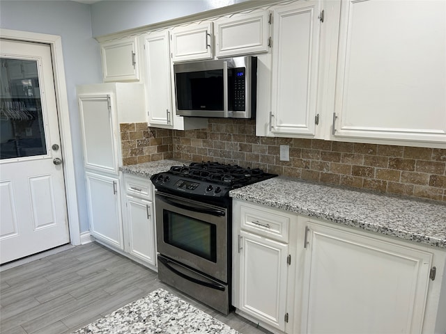 kitchen featuring decorative backsplash, appliances with stainless steel finishes, light stone counters, light hardwood / wood-style flooring, and white cabinetry