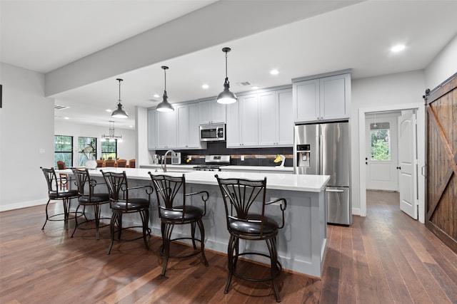 kitchen with stainless steel appliances, a barn door, dark hardwood / wood-style floors, a large island with sink, and decorative light fixtures