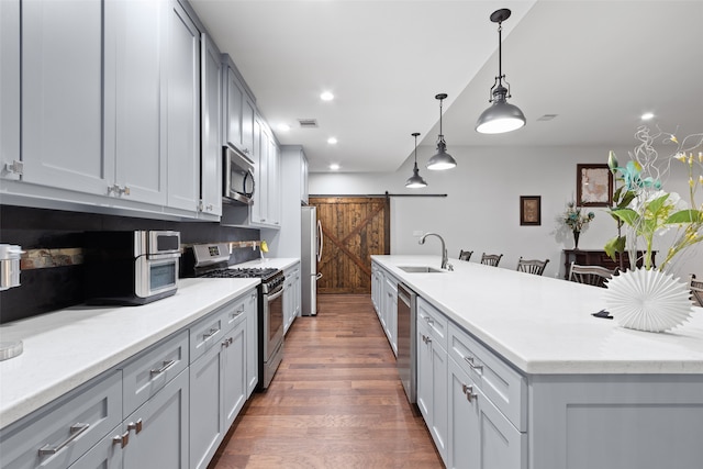 kitchen featuring a kitchen island with sink, dark wood-type flooring, sink, a barn door, and appliances with stainless steel finishes