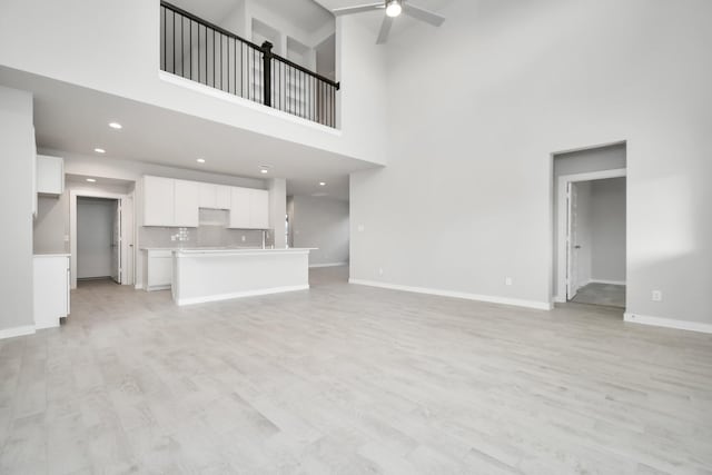 unfurnished living room featuring recessed lighting, ceiling fan, baseboards, light wood-type flooring, and a towering ceiling
