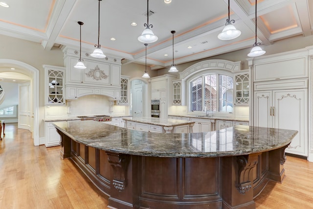 kitchen with a large island with sink, hanging light fixtures, light wood-type flooring, and dark stone countertops