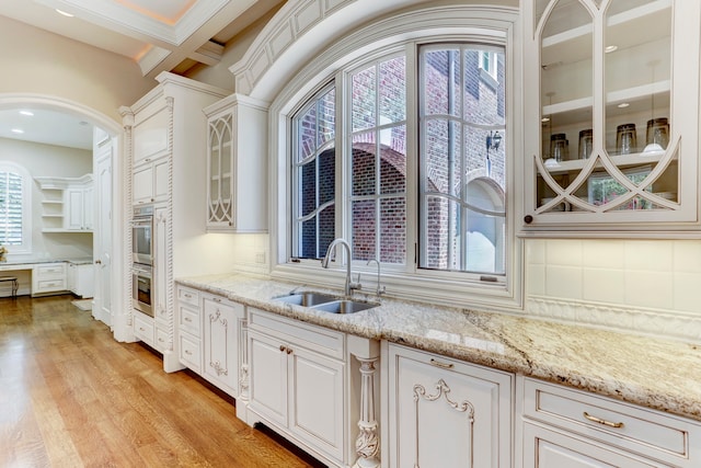 kitchen with light stone countertops, sink, backsplash, white cabinetry, and light hardwood / wood-style floors