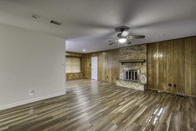 unfurnished living room featuring a textured ceiling, ceiling fan, wood walls, and a fireplace