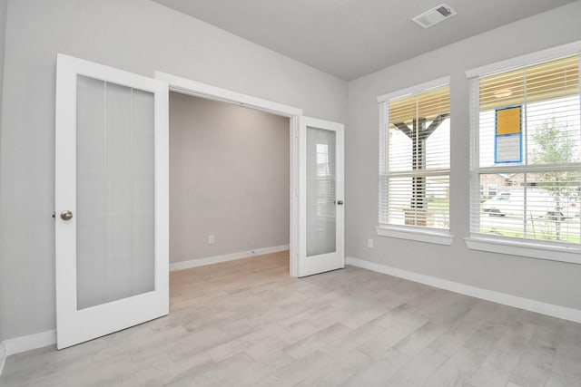 interior space featuring light wood finished floors, visible vents, multiple windows, and french doors