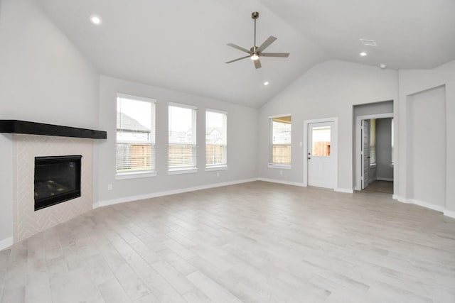 unfurnished living room with ceiling fan, a tiled fireplace, lofted ceiling, and light wood-style floors