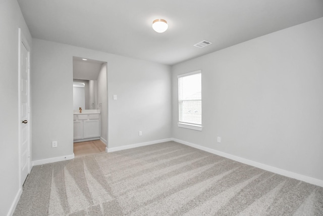 unfurnished bedroom with baseboards, visible vents, light carpet, and connected bathroom