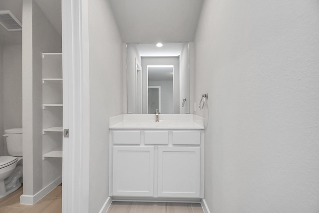bathroom with wood finished floors, toilet, vanity, baseboards, and visible vents