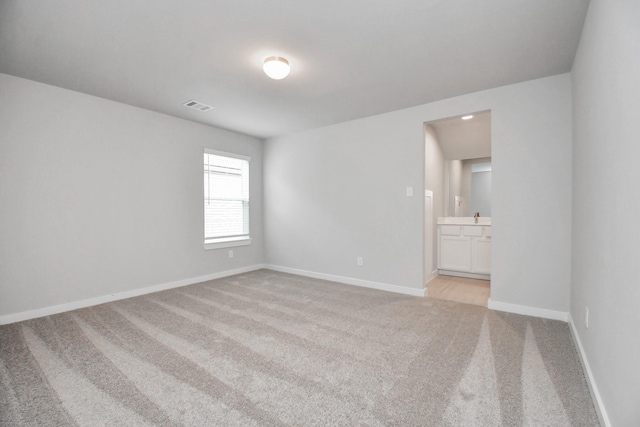 empty room with baseboards, visible vents, light colored carpet, and a sink