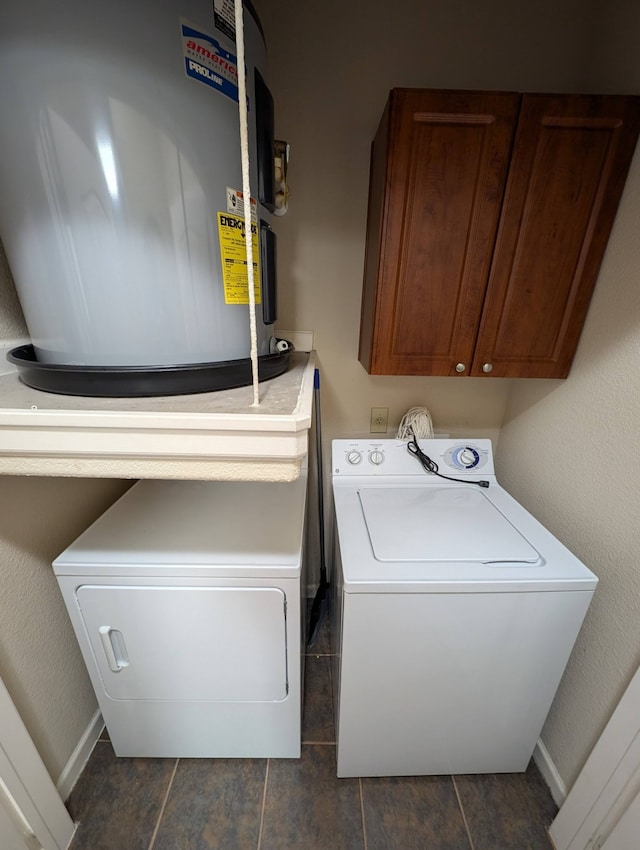 clothes washing area with washer and dryer, cabinets, water heater, and dark tile patterned floors