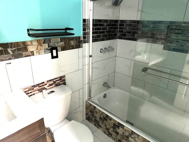 full bathroom featuring vanity, toilet, tile walls, and enclosed tub / shower combo