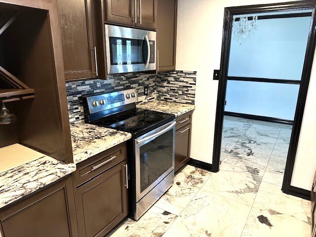 kitchen with dark brown cabinets, appliances with stainless steel finishes, light stone counters, and decorative backsplash