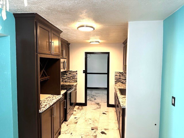 kitchen with decorative backsplash, light stone counters, stainless steel appliances, and a textured ceiling