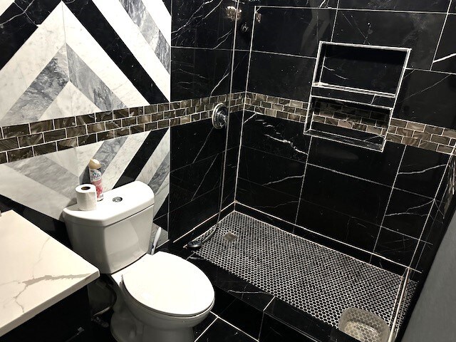 bathroom featuring vanity, tile walls, a tile shower, and toilet