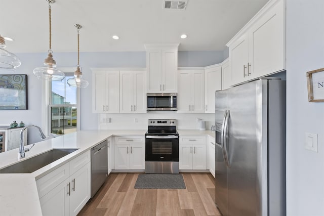 kitchen featuring appliances with stainless steel finishes, sink, hanging light fixtures, white cabinetry, and light hardwood / wood-style flooring