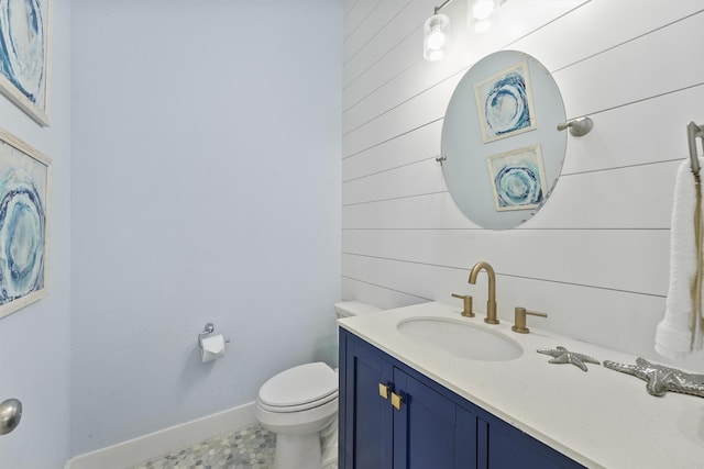 bathroom featuring toilet, vanity, and wooden walls