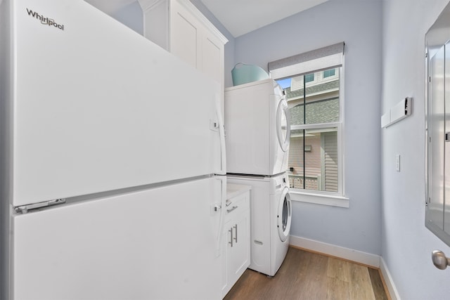 laundry room with a healthy amount of sunlight, cabinets, stacked washer and dryer, and dark hardwood / wood-style floors