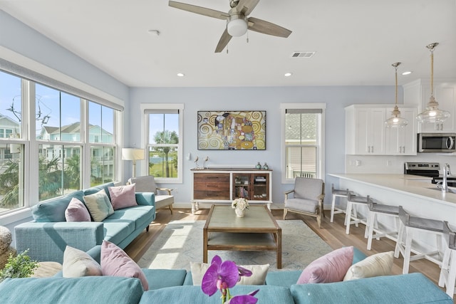 living room featuring ceiling fan, sink, and light wood-type flooring