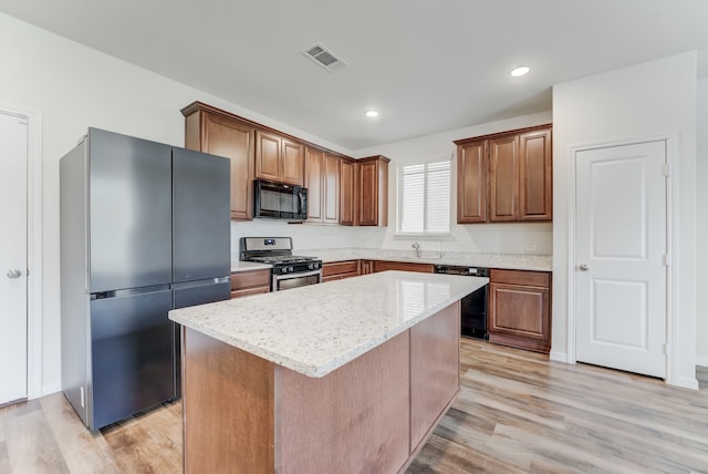 kitchen with light stone counters, black appliances, light hardwood / wood-style flooring, and a kitchen island