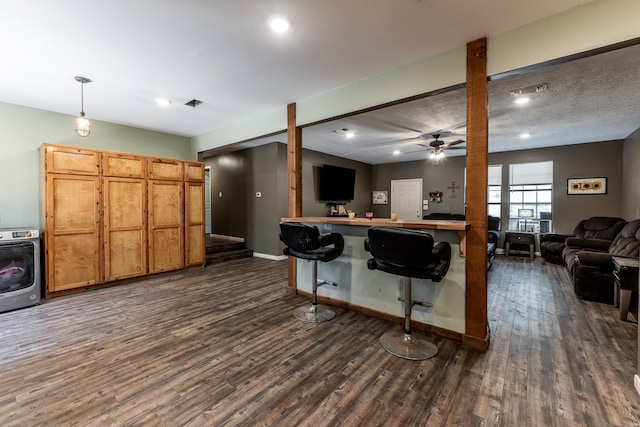 kitchen with washer / clothes dryer, ceiling fan, decorative light fixtures, dark wood-type flooring, and a breakfast bar area