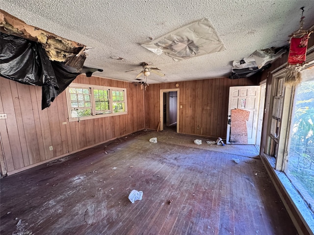 interior space with ceiling fan, wood walls, wood-type flooring, and a textured ceiling