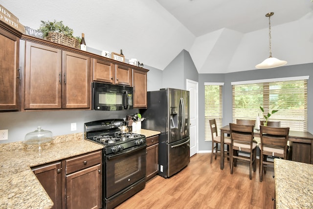 kitchen featuring light stone countertops, black appliances, hanging light fixtures, light hardwood / wood-style floors, and lofted ceiling