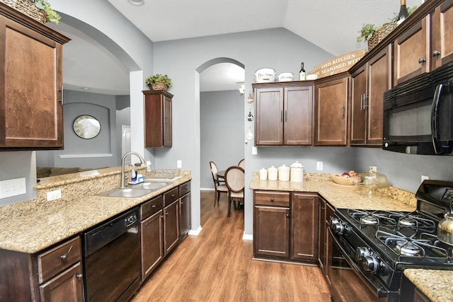 kitchen featuring lofted ceiling, light wood-type flooring, black appliances, sink, and light stone counters