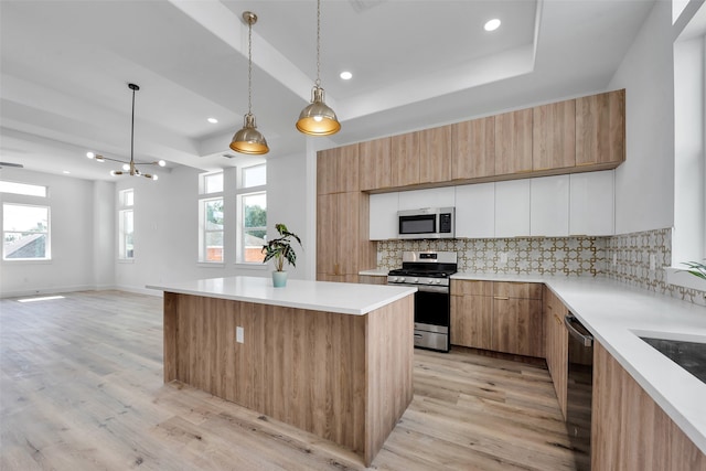 kitchen featuring light wood-style floors, appliances with stainless steel finishes, backsplash, and a tray ceiling