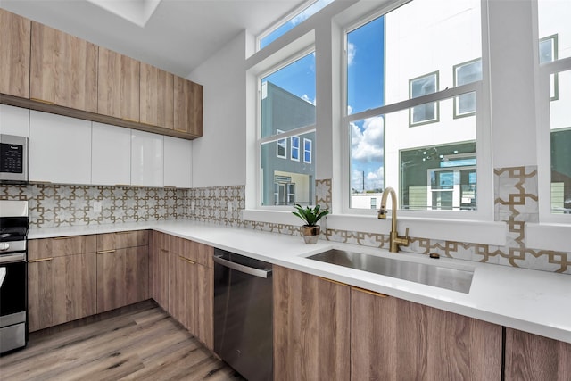 kitchen featuring decorative backsplash, modern cabinets, a sink, light countertops, and stainless steel appliances